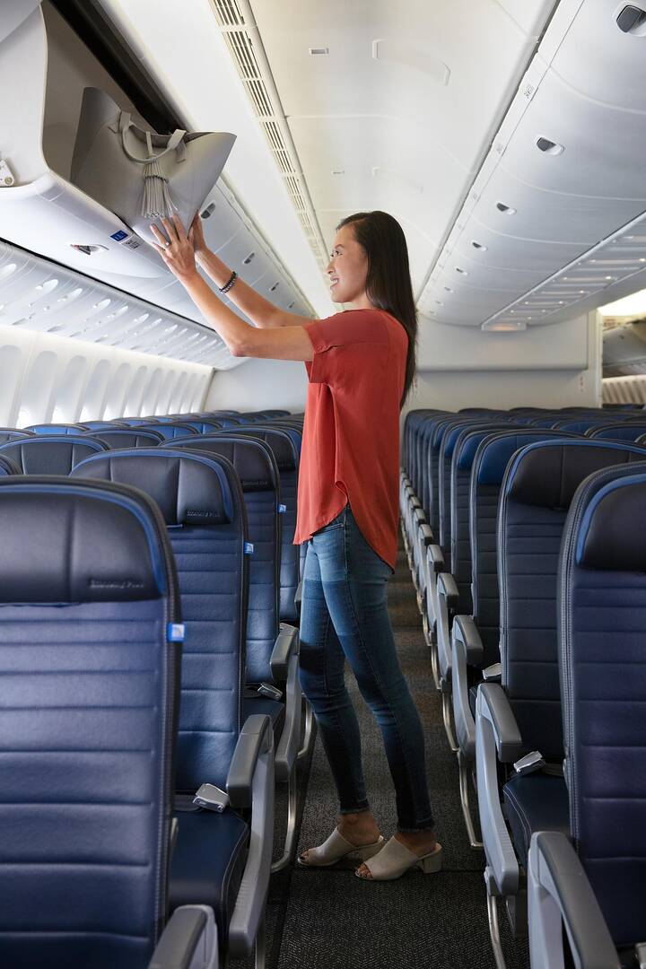 Image of woman loading baggage into overhead compartment on united airlines